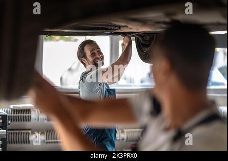 Fröhlicher Automobiltechniker und sein Kollege, der das Auto des Kunden repariert Stockfoto