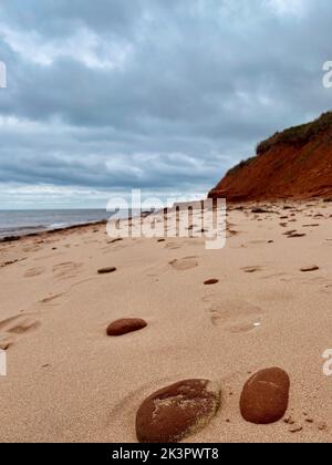 Die roten Sandsteinfelsen und der Sand am Cavendish Beach unter bewölktem Himmel, Prince Edward Island, Kanada Stockfoto