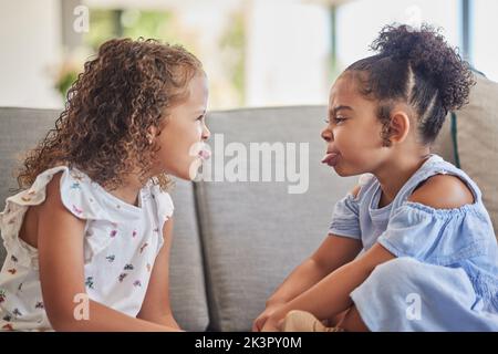 Lustige, verrückte und alberne Kinder spielen gerne und haben Spaß zusammen im Wohnzimmer Sofa zu Hause. Latino-Kinder oder -Schwestern ragen aus der Zunge und genießen es Stockfoto