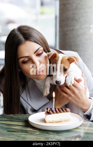 Kaukasische Frau und Jack russell Terrier schauen sich den Kuchen mit einer Kerze an. Der Hund und der Besitzer feiern den Geburtstag Stockfoto