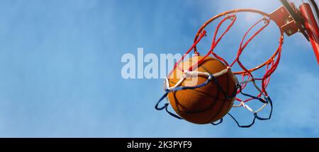 Basketball-Ball erzielte die Punkte vor blauem Himmel Hintergrund auf Outdoor-Streetball-Platz. Banner mit Copy Space Stockfoto