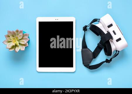 Weißes Tablet mit schwarzem Display, VR-Brille für Virtual-Reality-Spiele auf blauem Hintergrund Draufsicht Flat Lay Mock Up Technology Concept Platz zum Kopieren. Stockfoto