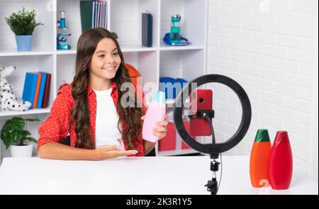 Junge Blogger Kind halten Haarspülung oder Shampoo-Flasche Aufnahme Video für Blog. Teen Mädchen sprechen vor der Kamera für vlog. Teenager arbeiten Stockfoto