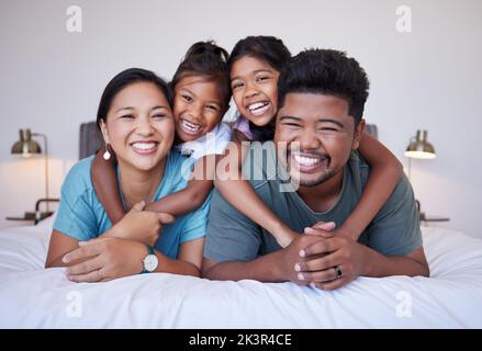 Porträt einer glücklichen asiatischen Familie auf dem Bett mit einem Lächeln im Gesicht. Multikulturelle indische Familie im Schlafzimmer lächelt, lacht und hat Spaß Stockfoto