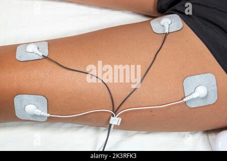 Frau in den 40er Jahren, die zu Hause eine TENS-Therapie (transkutane elektrische Nervenstimulation) und eine EMS-Therapie (elektronische Muskelstimulation) auf dem Muskel verwendete Stockfoto