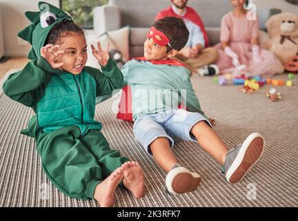 Familie, halloween und Kinder, die in Kostümen auf einem Boden im Wohnzimmer spielen, Spaß haben und kreativ sein. Superhelden, Dinosaurier und kreative Kinder Stockfoto