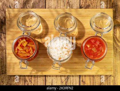 Rustikale Lebensmittelzusammensetzung mit probiotischen Lebensmitteln. Eingelegtes oder fermentiertes Gemüse. Lecho, Sauerkraut, Ajvar in Glasgefäßen auf Holzboden mit shado Stockfoto