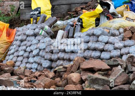 Eine Gartenrückhaltewand aus recycelten, vier Liter großen Milchbehältern aus Kunststoff, gefüllt mit Sand. Die Öko-Ziegel sind eine effektive Retention Gabion Stockfoto