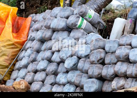 Eine Gartenrückhaltewand aus recycelten, vier Liter großen Milchbehältern aus Kunststoff, gefüllt mit Sand. Die Öko-Ziegel sind eine effektive Retention Gabion Stockfoto