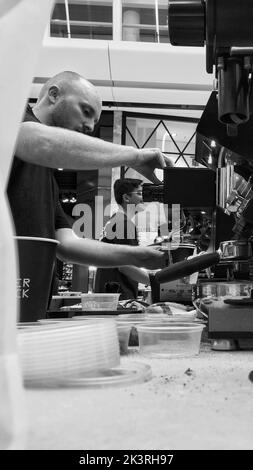 Eine vertikale Graustufenaufnahme von Baristas, die in einem Café Kaffee machen Stockfoto