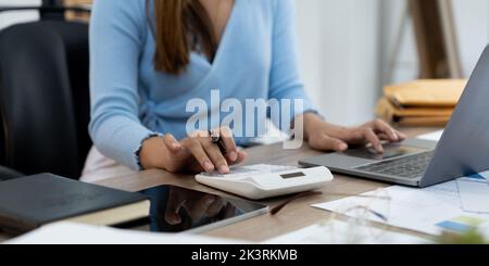 Frau hält den Stift in der Hand und verwendet den Rechner, um die Finanzen auf dem Schreibtisch im Heimbüro zu erledigen Stockfoto