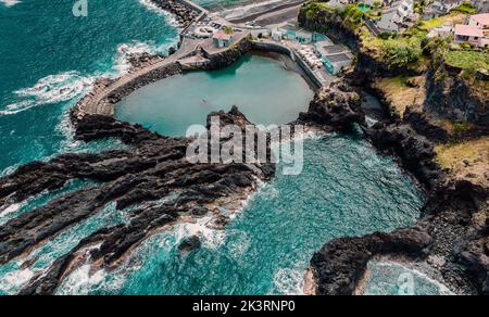 Natürliche Schwimmbäder und kleine Stadt auf Klippen, Atlantikküste. Madeira, Portugal. Luftdrohnenfotografie Stockfoto