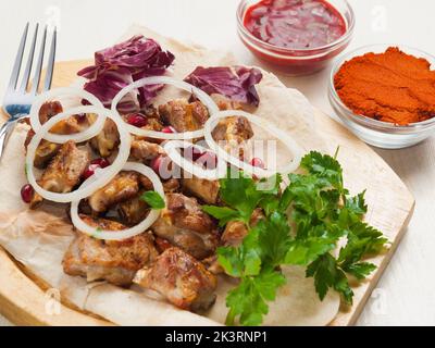 Leckere Lammstücke auf dem Knochen mit Zwiebeln und Saucen auf einem Holzbrett Stockfoto