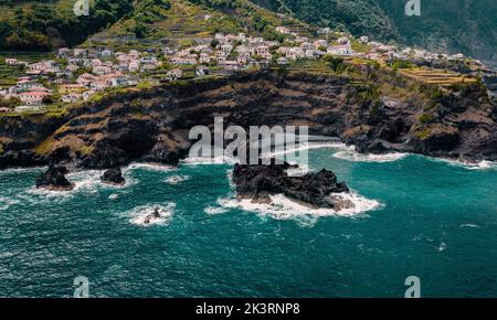 Kleine Stadt Seixal auf Klippen, Atlantikküste. Leerer Strand, Meeresschaum und Wellen. Madeira, Portugal. Luftaufnahmen von Drohnen Stockfoto