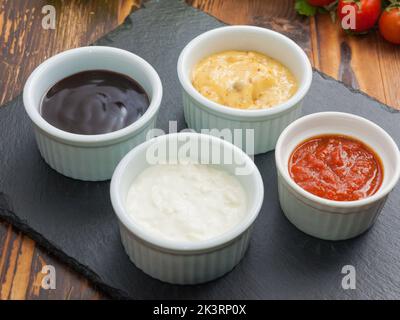 Beliebte Saucen: Käse Knoblauch und Tomaten, in kleinen Untertassen auf einem schwarzen Steinständer Stockfoto