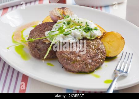 Zwei leckere Rindersteaks mit Kartoffeln, Spiegelei und gebackenen Zwiebeln auf einem weißen Teller Stockfoto