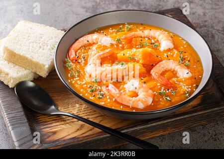 Kürbis-Gemüsesuppe mit Garnelen, Sesam und Thymian in Nahaufnahme auf einem Holztablett auf dem Tisch. Horizontal Stockfoto