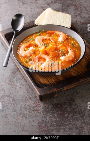 Kürbispüree-Suppe mit Garnelen, Sesam und Thymian, serviert mit Brot auf einem Holztablett auf dem Tisch. Vertikal Stockfoto
