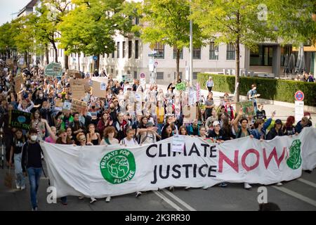 Jubelnde Teilnehmer*innen hinter Banner 'Klimagerechtigkeit jetzt!'. Am 23.9.2022 sammeln sich in München bis zu 10,000 Menschen, um gemeinsam mit Fridays for future auf dem globalen Klimabereich für Klimagerechtigkeit, den Ausbau der dezentralen erneuerbaren Energien, kostengünstigen ÖPNV und für ein 100 Mrd. Euro Sondervermögen für gerechte Klimaschutzmaßnahmen und Krisenprävention zu demontieren. Das Motto des Großstreiks war wieder People Not Profit. -- jubelnde Teilnehmer hinter dem Banner "Climate Justice Now! Am 23. September 2022 versammelten sich bis zu 10.000 Personen in München Stockfoto