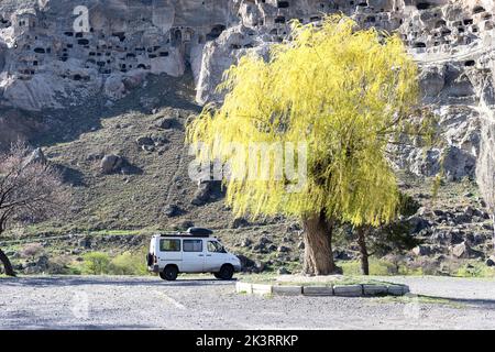 Ein Geländewagen parkt an der wunderschönen Weide in vollen Frühlingsfarben mit dem Höhlenkloster Vardzia auf der Rückseite, Georgia Stockfoto