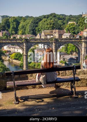 Frau, die auf einer Bank sitzt und den Blick auf den Eisenbahnviadukt über den Fluss Nidd in Knaresborough North Yorkshire England genießt Stockfoto