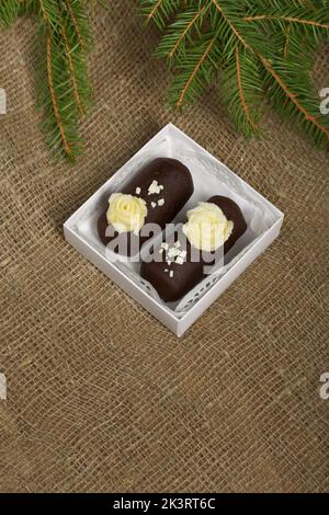 Tortenkartoffel. Dekoriert mit Buttercreme. In einer Geschenkbox. Auf Leinenhintergrund. Neben einem Fichtenzweig. Nahaufnahme. Stockfoto