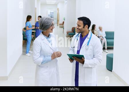 Rat der Ärzte. Reife Hausärztin kommuniziert mit dem indischen Arzt, während sie tagsüber im Krankenhaus steht Stockfoto