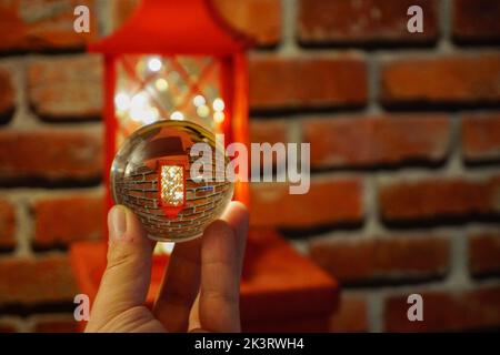 Eine Glaskugel mit umgekehrter Reflexion in der Hand vor einem Backstein-Hintergrund. Stockfoto