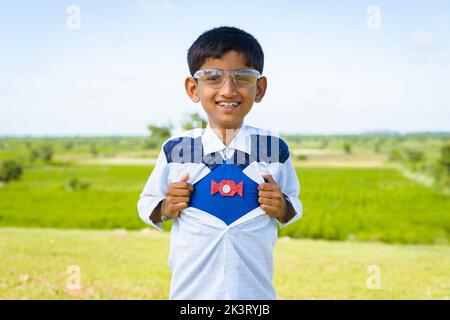 Glücklich lächelndes indisches Teenager-Kind zeigt Supermacht durch Ausziehen des Hemdes durch Blick auf die Kamera - Konzept der Inspiration, Stärke und Glück. Stockfoto