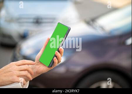 Frau mit Smartphone, die neben dem Auto steht, die mobile App für die Online-Kommunikation nutzt, shpping Stockfoto