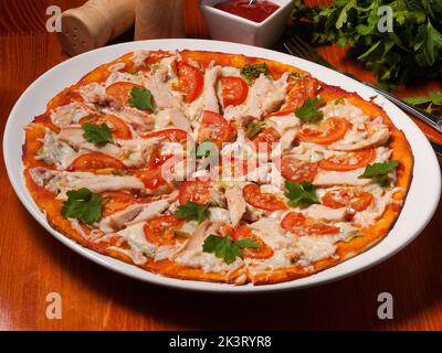 Leckere Pizza Caesar auf einem weißen Teller auf einem Holztisch mit Tomatensauce Stockfoto