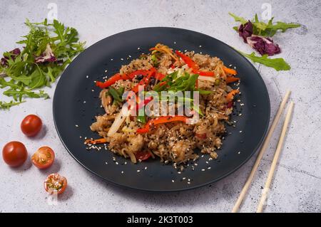 Schmackhafter gebratener Reis mit Gemüse auf einem schwarzen Teller. Asiatische Küche Stockfoto