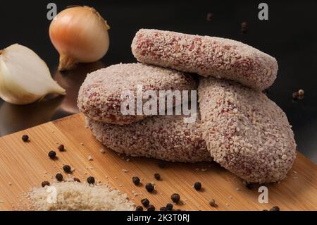 Leckere rohe Schweinekoteletts mit Zwiebeln in Paniermehl Stockfoto