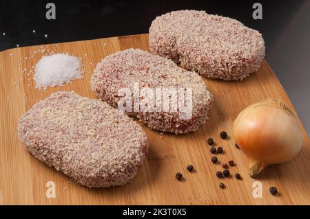 Leckere rohe Koteletts mit Zwiebeln in Paniermehl auf einem Holzbrett Stockfoto