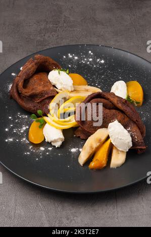 Süße Schokoladenpfannkuchen mit Obst und Quark auf einem dunklen Teller Stockfoto