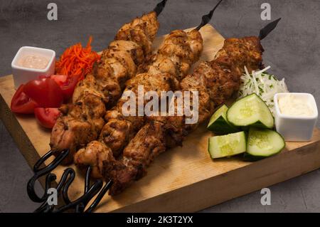 Leckere, sortierte Kebabs auf Metallspiessen mit Gemüse und Saucen Stockfoto