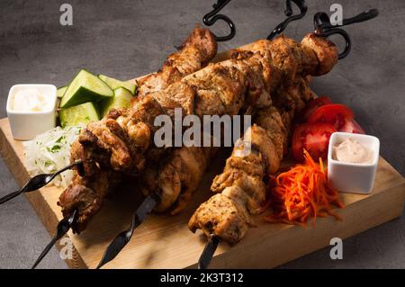 Leckere, sortierte Kebabs auf Metallspiessen mit Gemüse und Saucen Stockfoto