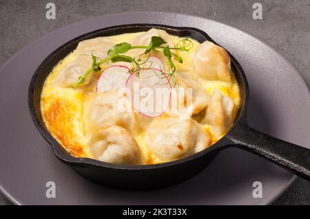 Leckere Knödel, die in einem Omelett in einer Pfanne gebacken werden und mit Radieschen und Mikrogemüse dekoriert sind Stockfoto