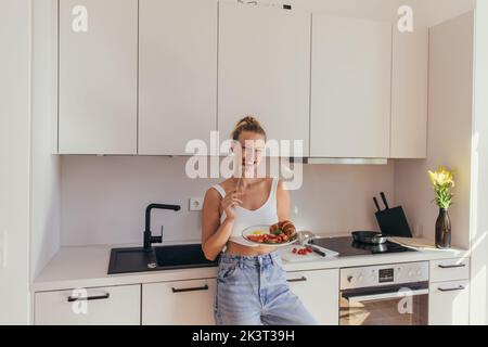 Lächelnde Frau, die Kirschtomate isst, während sie in der Küche frühstücken, Stockbild Stockfoto