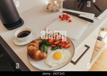 Köstliches Frühstück mit Ei und Croissant in der Nähe von Kaffee in der Küche, Stock Bild Stockfoto