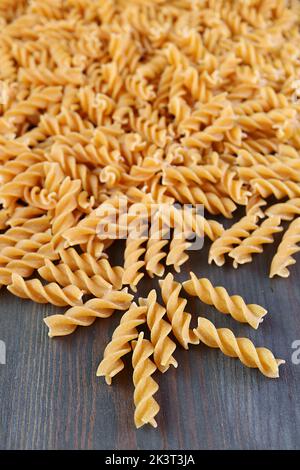 Haufen ungekochte ganze Weizen Fusilli Pasta auf schwarzem Holzhintergrund verstreut Stockfoto