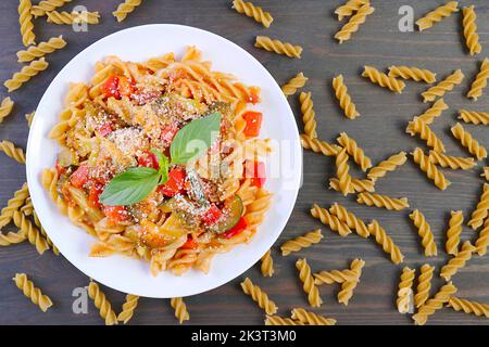 Draufsicht auf einen Teller mit köstlicher Fusilli-Pasta in Tomatensauce mit getrockneten Pasta, die verstreut sind Stockfoto