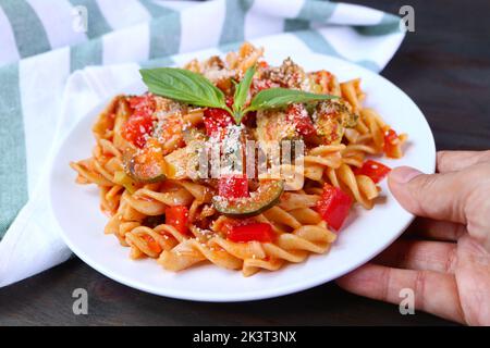 Eine Platte mit köstlicher Fusilli Pasta in Marinara-Sauce von Hand auf einen Holztisch legen Stockfoto