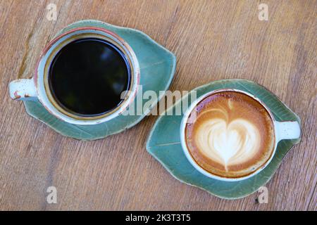 Blick von oben auf schwarzen Kaffee und heißen Cappuccino auf Holztisch Stockfoto