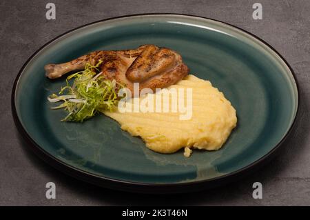 Wachtel mit Kartoffelpüree auf einem grünen Teller auf grauem Hintergrund Stockfoto