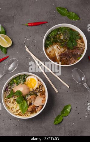 Ein Stillleben mit leckeren asiatischen Ramen-Suppen und einem Foto auf grauem Hintergrund in handwerklichen Gerichten. Konzept: Lebensmittelzustellung, Street Food Stockfoto