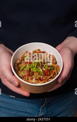 Ein Mann hält eine Schüssel mit leckeren udon-Nudeln mit Huhn und Gemüse Stockfoto