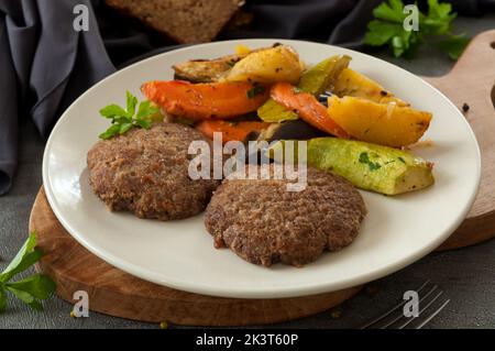 Leckere Rindfleischpasteten mit gebackenem Gemüse auf einem grauen Teller Stockfoto