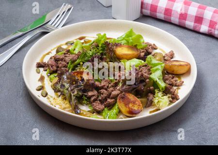Schmackhafter warmer Salat mit Kartoffeln, Leber und eingelegter Gurke Stockfoto