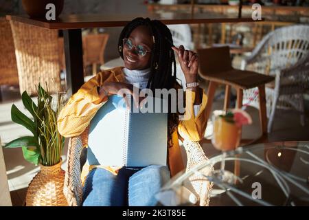 Ein afrikanischer Student, der in einem Café sitzt und für die Abschlussprüfung studiert. Hochschulbildung und Studentenleben. Stockfoto